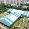 Aerial view sports marquee complex - green white striped clear span tent, basketball facility, drone shot